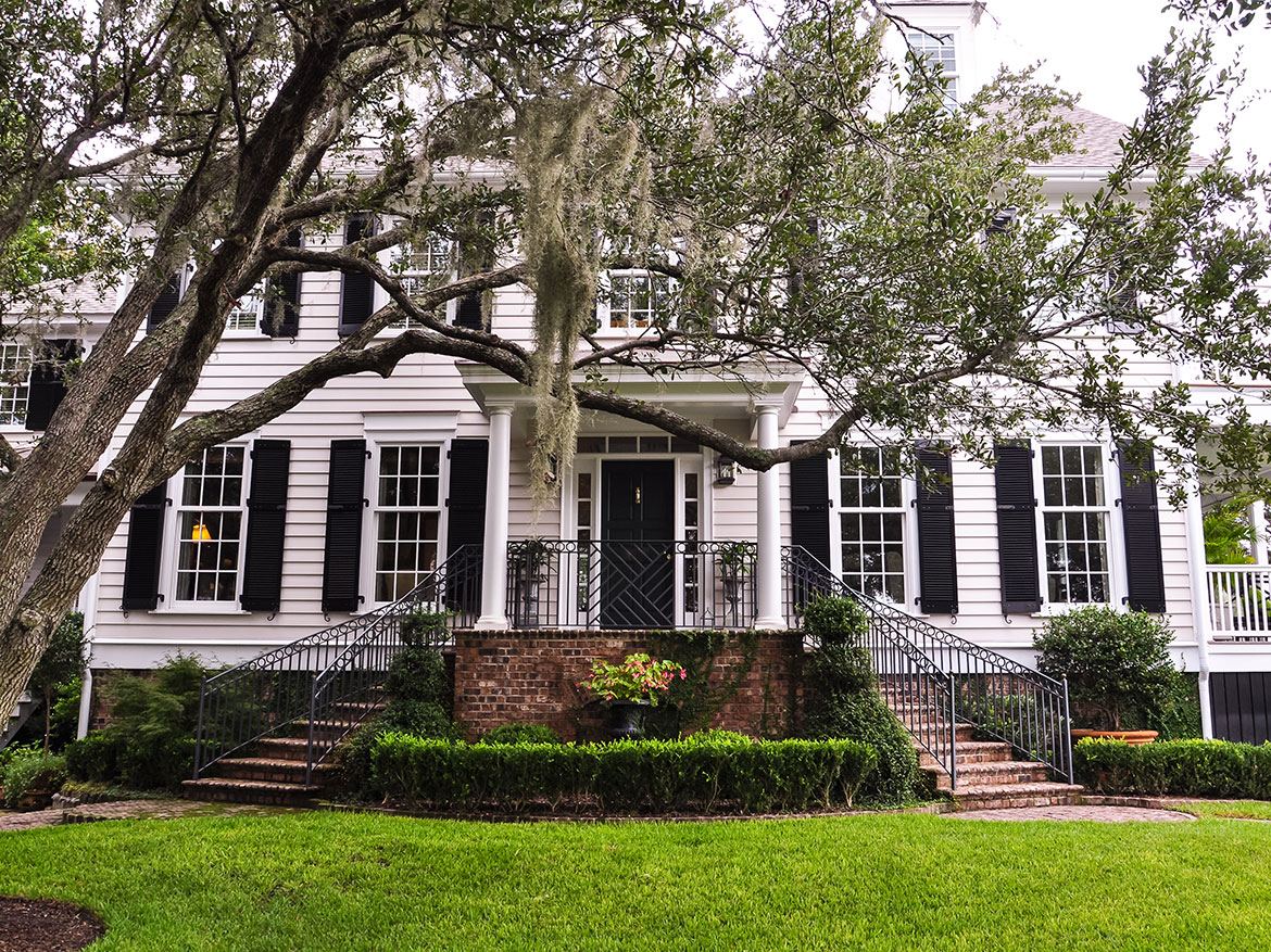 A white house with black shutters and a large tree | apartments in gurgaon